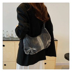 Detail van gewassen denim schoudertas met geplooide onderkant en zilveren klinknagels