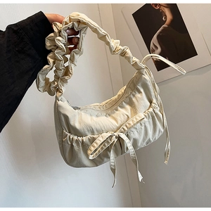 Close-up of beige nylon crescent bag featuring ruffled shoulder strap and bow detail