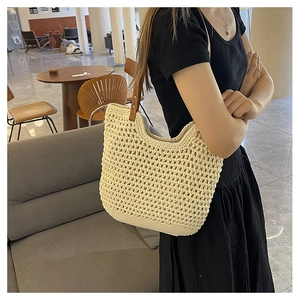 Detail of a cream crochet hollow tote bag with brown leather straps worn on shoulder