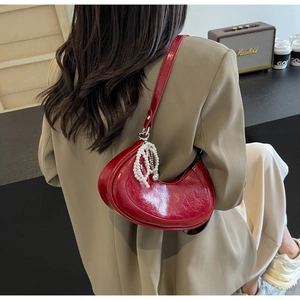 Detail of red crescent moon shoulder bag with glossy texture and pearl charm on a model