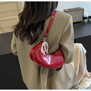 Detail of red crescent shoulder bag with glossy patent texture and pearl tassel charm