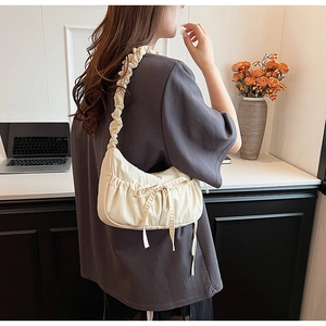 Detail view of a cream pleated underarm bag with a bow and ruched shoulder strap
