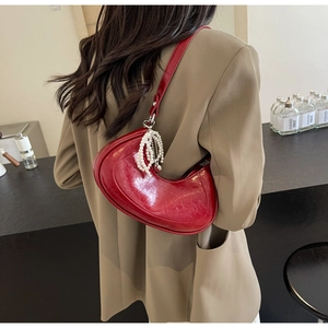 Detail view of red glossy patent leather crescent bag with elegant white pearl strap charm