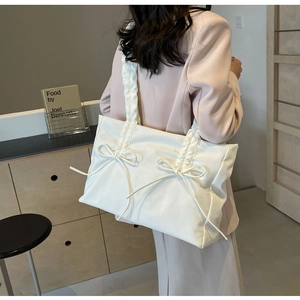 Detail van een beige draagtas met decoratieve strikken en een geplooide schouderband