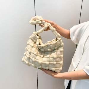 Detail of creamy white woven puff shoulder bag featuring knot handle and 3D grid texture