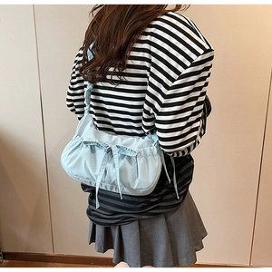 Detail of light blue pleated canvas bag featuring a decorative bow knot and crossbody strap