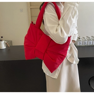 Side view of a bright red oversized bow shoulder bag with padded nylon texture