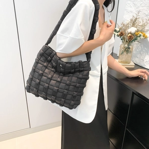 Close-up of black quilted puffer shoulder bag showing woven texture and wide strap on model