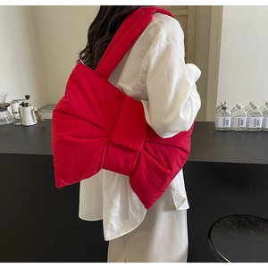 Macro shot of a vibrant red 3D bow-shaped nylon shoulder bag worn over a white shirt