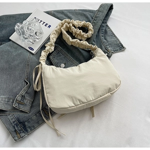 Detail of cream canvas dumpling bag with ruched strap on denim background