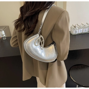 Close-up of silver crescent handbag with metallic pleats and elegant pearl strap charm