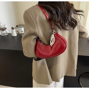 Detail of red crescent shoulder bag featuring glossy finish and pearl tassel charm