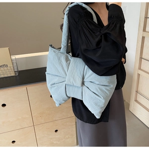 Side view of light blue fabric bow-shaped shoulder bag shown on a female model