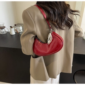 Close-up of red glossy pleated leather crescent bag with decorative pearl chain detail