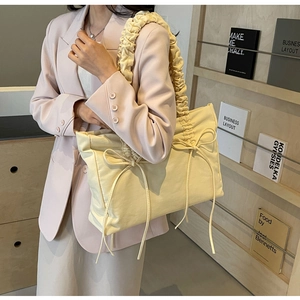 Detail van de crèmegele nylon draagtas met geplooide bandjes en decoratieve strikaccenten