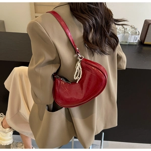 Detail of red patent leather crescent bag with pearl charm on a khaki blazer