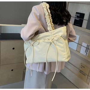 Detail van een crèmegele nylon draagtas met decoratieve strikken en een geplooide schouderband