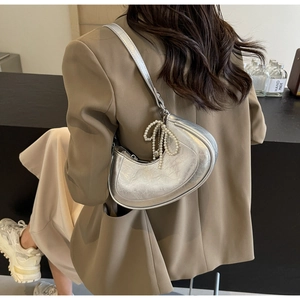 Silver crescent bag with pleated texture and pearl bow charm shown on model's shoulder