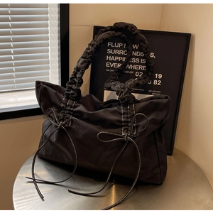 Detailweergave van de zwarte nylon draagtas met geplooide hengsels en strikdetails