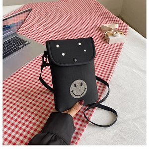 Detail of black mini crossbody bag featuring a rhinestone smiley face and silver metal rivets