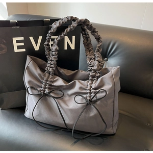 Detail van grijze shopper met geplooide handvatten en decoratieve strikjes op de bank