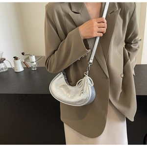 Silver crescent bag with pearl bow pendant worn by a model in a minimal cafe setting