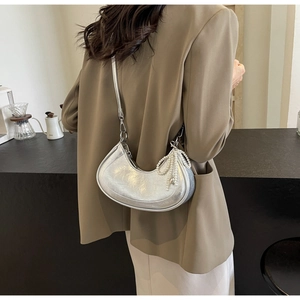 Silver half-moon shoulder bag with pearl bow charm shown in a modern cafe setting