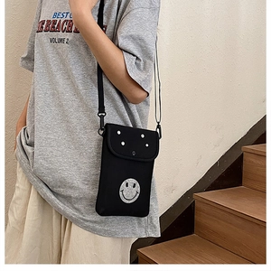 Detail of black crossbody phone bag featuring a rhinestone smiley face and metal studs