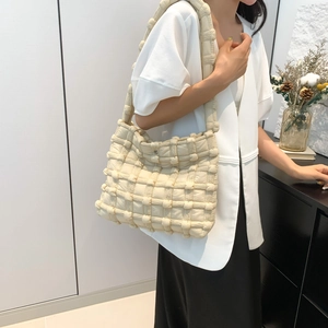 Creamy white quilted puffy shoulder bag with soft woven texture in a minimalist setting