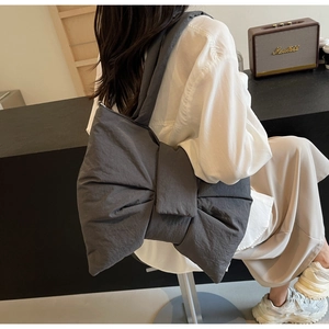 Detail view of stylish grey nylon shoulder bag with a large decorative bow on model