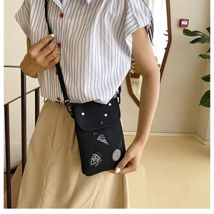 Detail of black crossbody phone bag with sequin rose patches on casual striped shirt