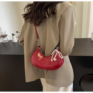 Detail of red glossy half-moon hobo bag with pearl bow and heart charm on a shoulder