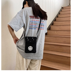 Detail of a black canvas crossbody phone bag featuring a white smiley face on the flap