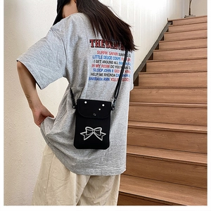 Model view of a black canvas crossbody phone bag with bow embroidery and adjustable strap