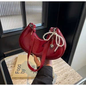 Detail of red patent leather crescent bag with pearl bow charm and heart pendant