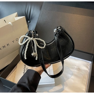 Detail of black glossy leather crescent bag featuring a pearl bow and silver heart pendant