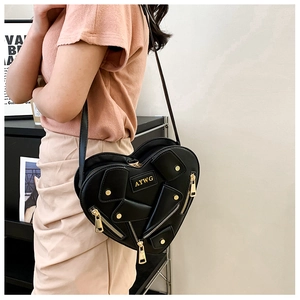 Detail of a black heart-shaped crossbody bag with gold zippers and biker style metal rivets