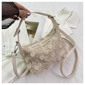 Close-up of beige sequin handbag featuring a metallic zipper and slender leather handle