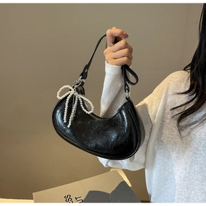 Close-up of black pleated dumpling bag with elegant pearl bow charm and silver zipper