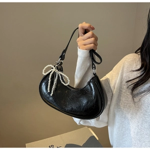 Detail of black crescent bag with pearl bow charm and wrinkled patent leather texture