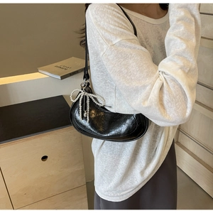 Detail of black croissant shoulder bag featuring a pearl bow charm and wrinkled texture