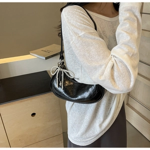Detail of black pleated leather crescent bag with pearl bow charm shown on model