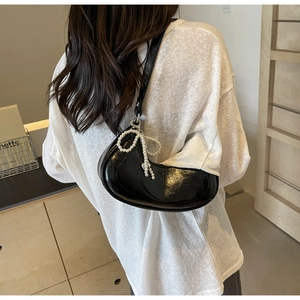 Detail view of black crescent shoulder bag with glossy leather and pearl bow charm