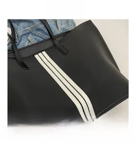 Detail of the black nylon tote bag with three vertical white stripes and slim handles