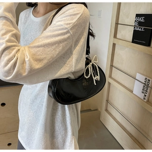 Detail of black crescent shoulder bag with pearl bow charm and glossy leather texture