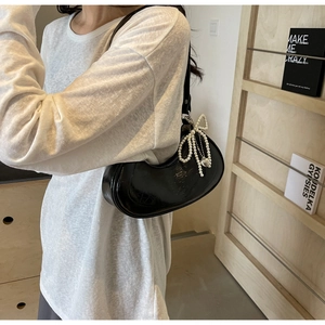 Detail of black glossy crescent shoulder bag with pearl bow charm on model