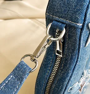 Detail of silver metal buckles and white stitching on blue denim guitar shoulder bag