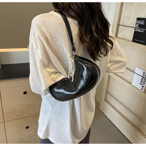 Close-up of black glossy leather crescent bag featuring elegant pearl chain charm detail