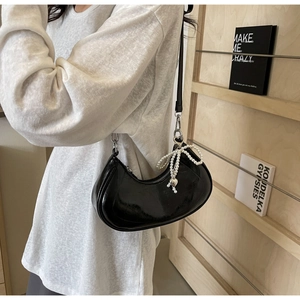 Detail of black patent leather half-moon bag with pearl bow and silver heart charm