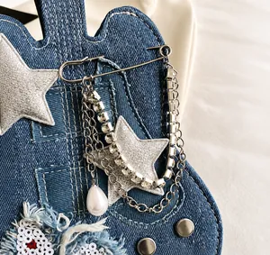 Detail of star-shaped pin with metal chains and pearls on blue denim fabric